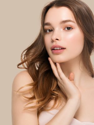 Young girl with care beautiful healthy clean skin and hand touching face. Color background. Brown